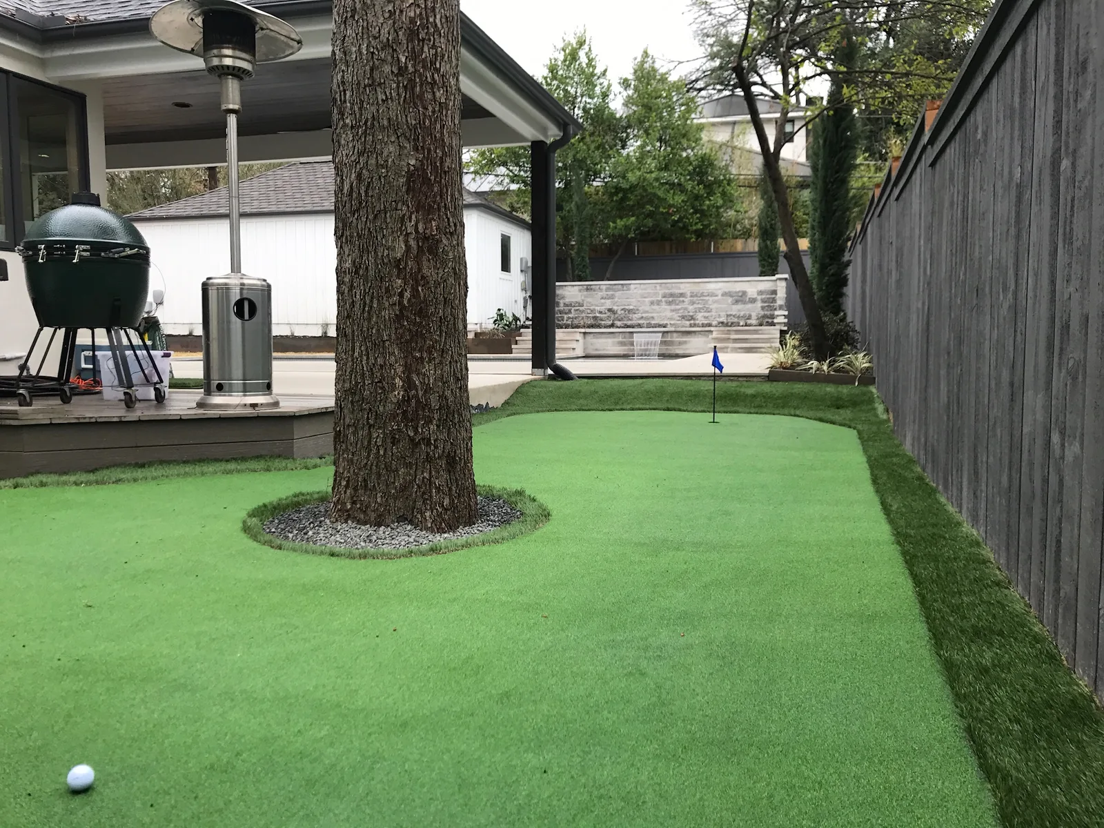 Compact backyard putting green built around a live oak next to a covered patio