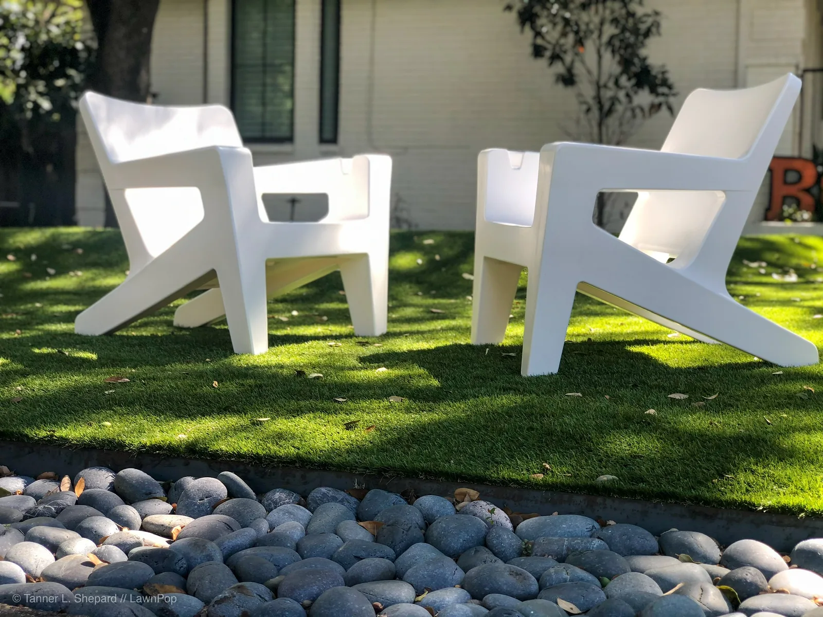 White lounge chairs on artificial turf with a river-rock border