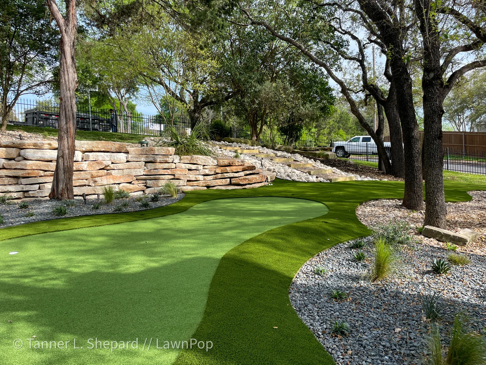 Contoured putting green with rough-style fringe between limestone walls and oaks