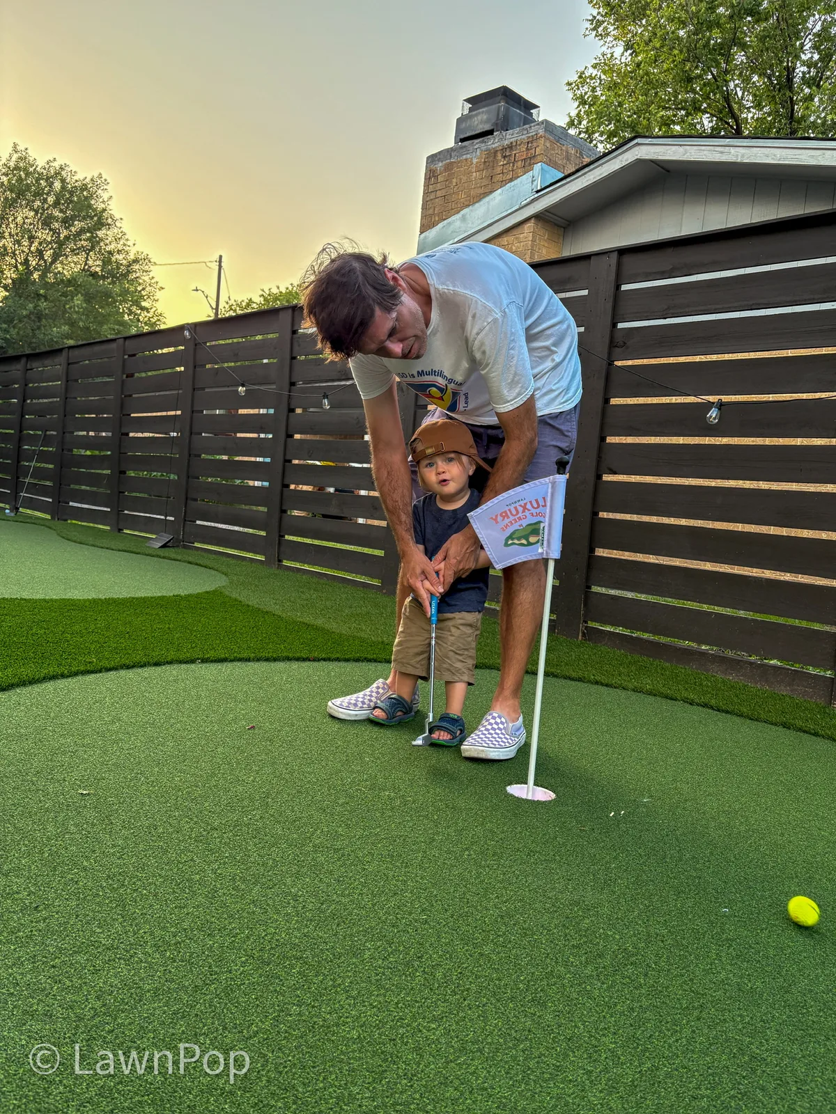 Father teaching his young son to putt on their backyard putting green