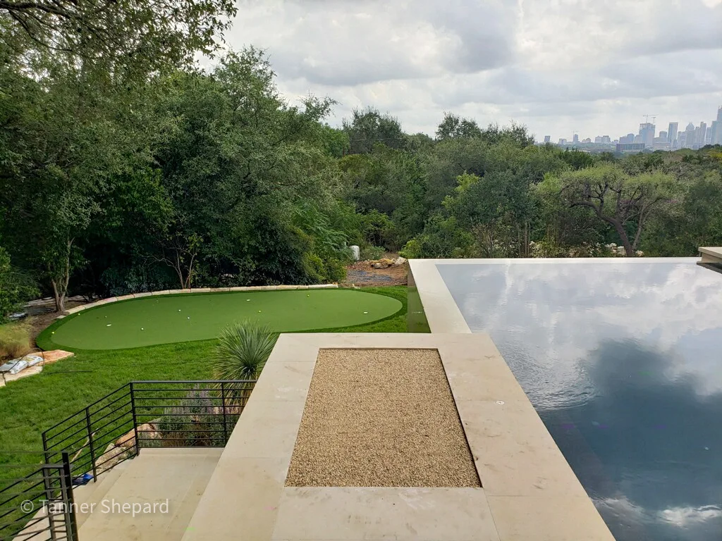 Putting green beside an infinity pool with the Austin skyline in the distance