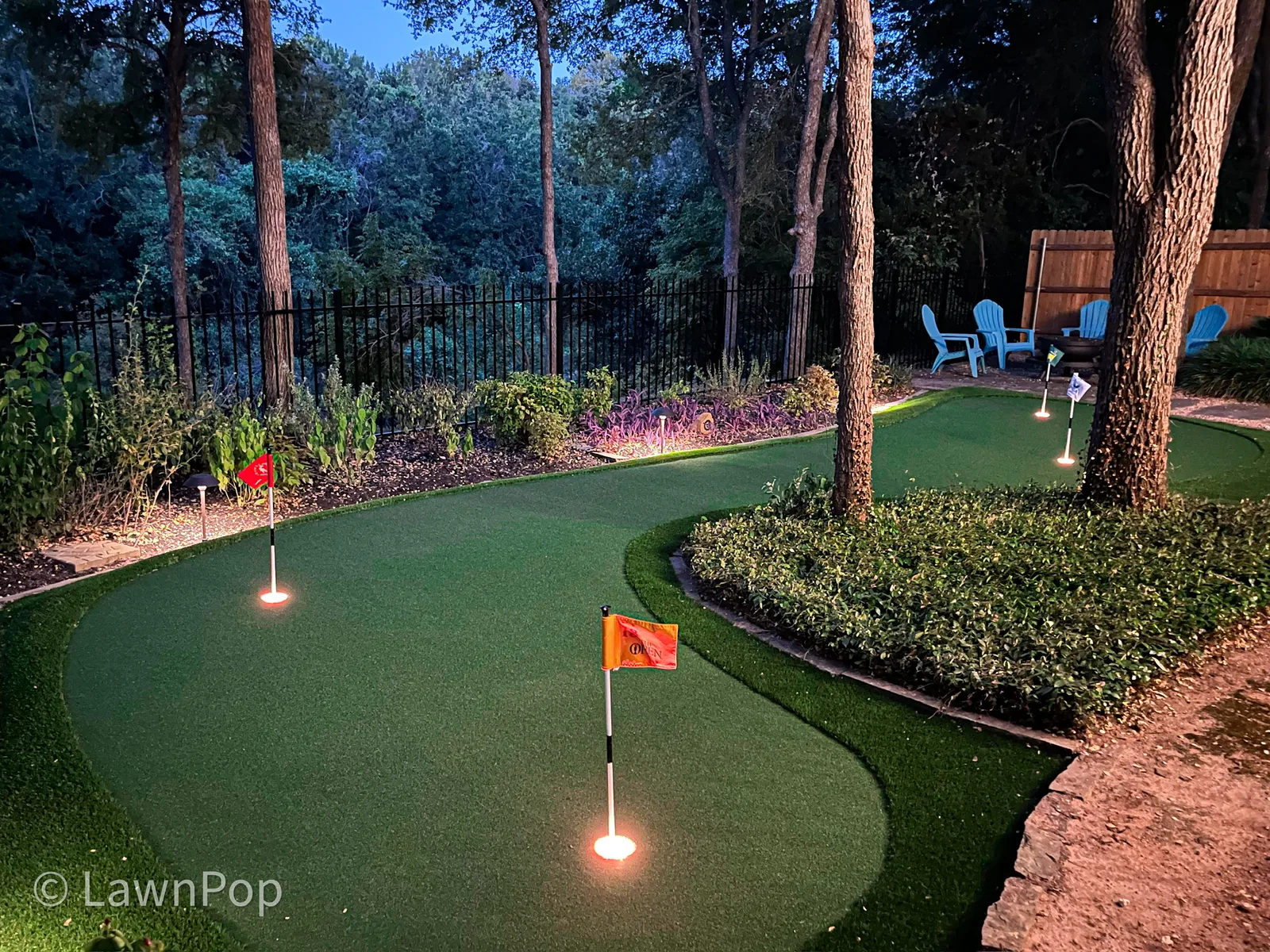 Backyard putting green at night with illuminated cups and landscape lighting