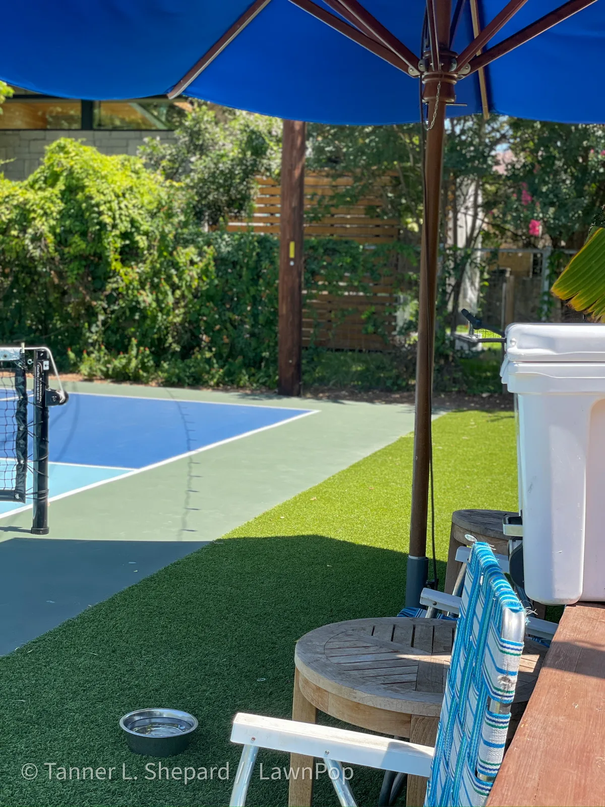 Backyard pickleball court beside artificial turf with shade sails
