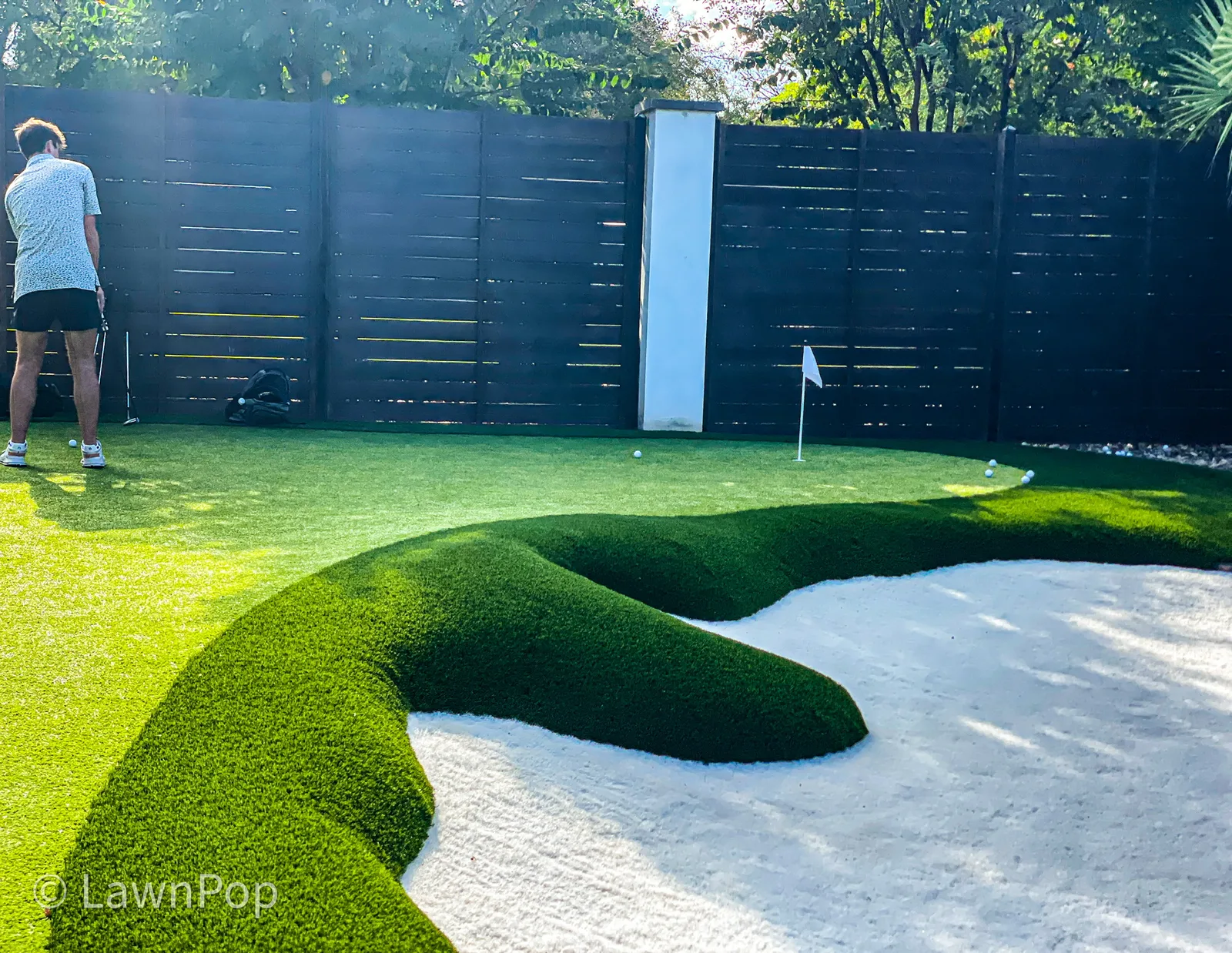 Golfer practicing a chip shot from a white turf bunker on a backyard putting green
